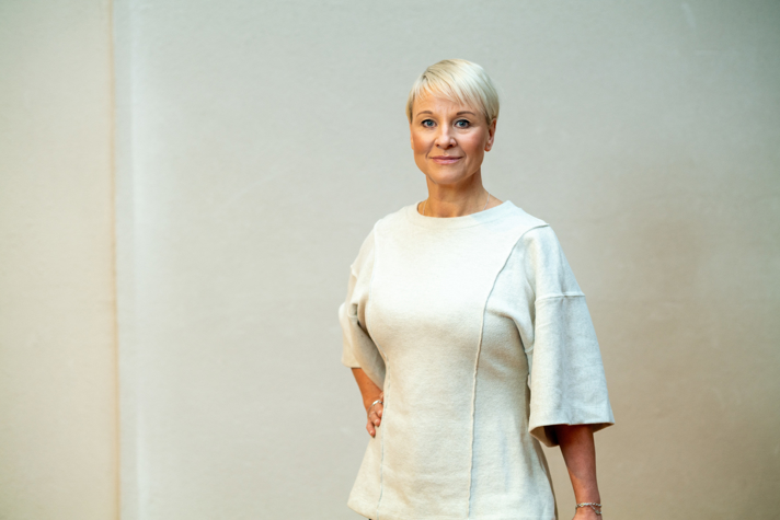 Äldre- och socialförsäkringsminister Anna Tenje i vit klänning vänd mot kameran.